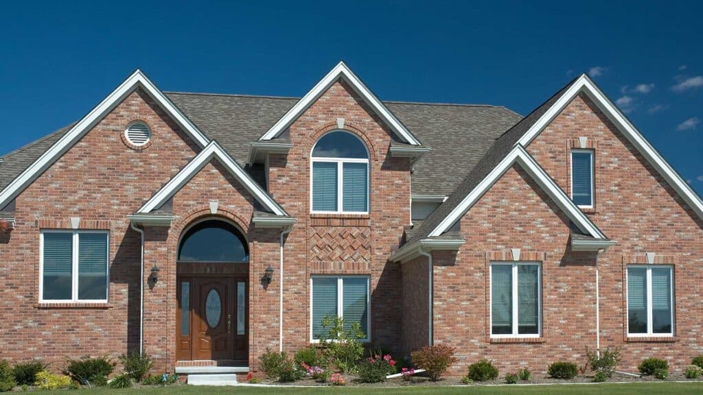 Red brick two-story home with a gray architectural shingle roof, steep gables and an arched front entry