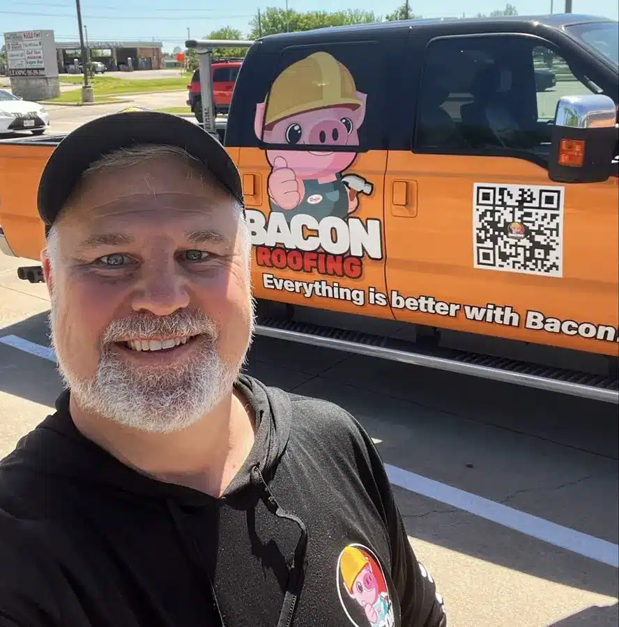 John Bacon, owner of Bacon Roofing, standing in front of an orange company truck with the Roofus pig logo